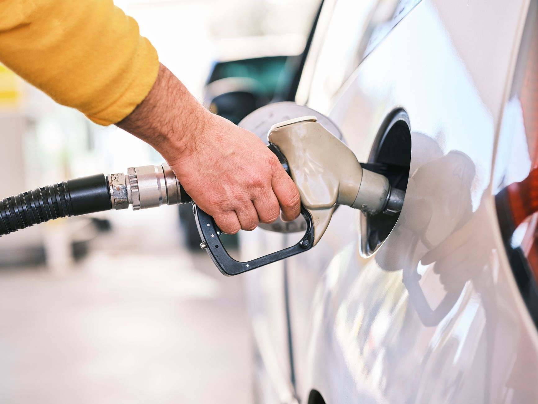 Une main tient un pistolet de distribution de carburant pour remplir le réservoir d'une voiture blanche.
